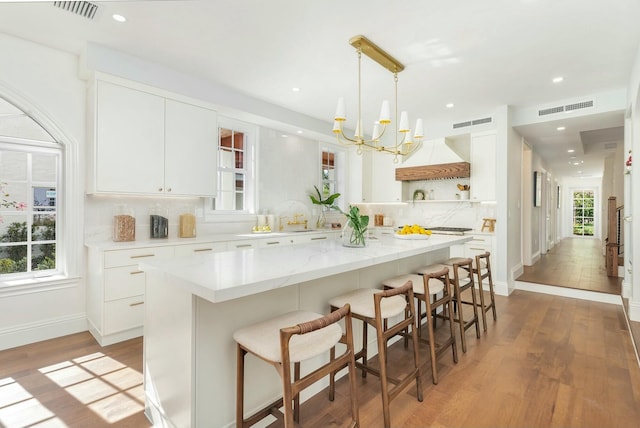 kitchen with white cabinets, hanging light fixtures, hardwood / wood-style flooring, decorative backsplash, and a breakfast bar area