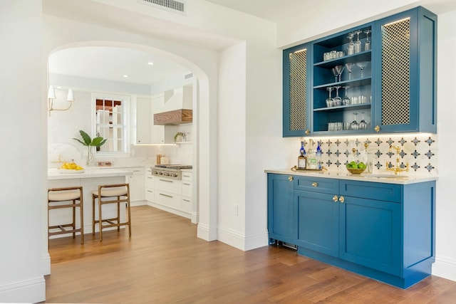 bar featuring custom range hood, light wood-type flooring, white cabinetry, and blue cabinets