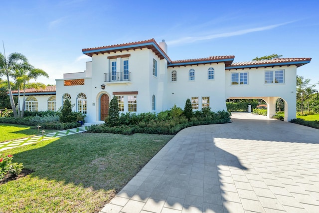 mediterranean / spanish-style house with a carport, a balcony, and a front lawn