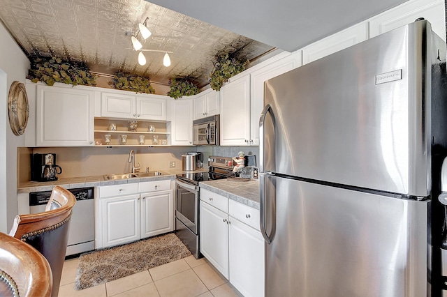 kitchen with sink, appliances with stainless steel finishes, tile counters, light tile patterned flooring, and white cabinetry