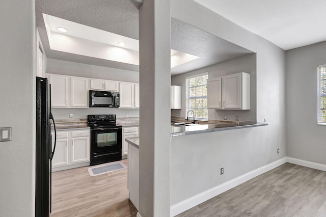 kitchen with white cabinets, black appliances, a textured ceiling, and light wood-type flooring