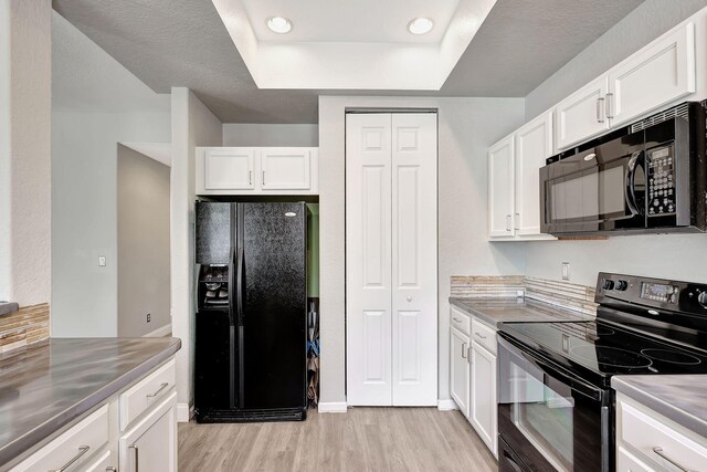 kitchen with stainless steel counters, white cabinets, and black appliances