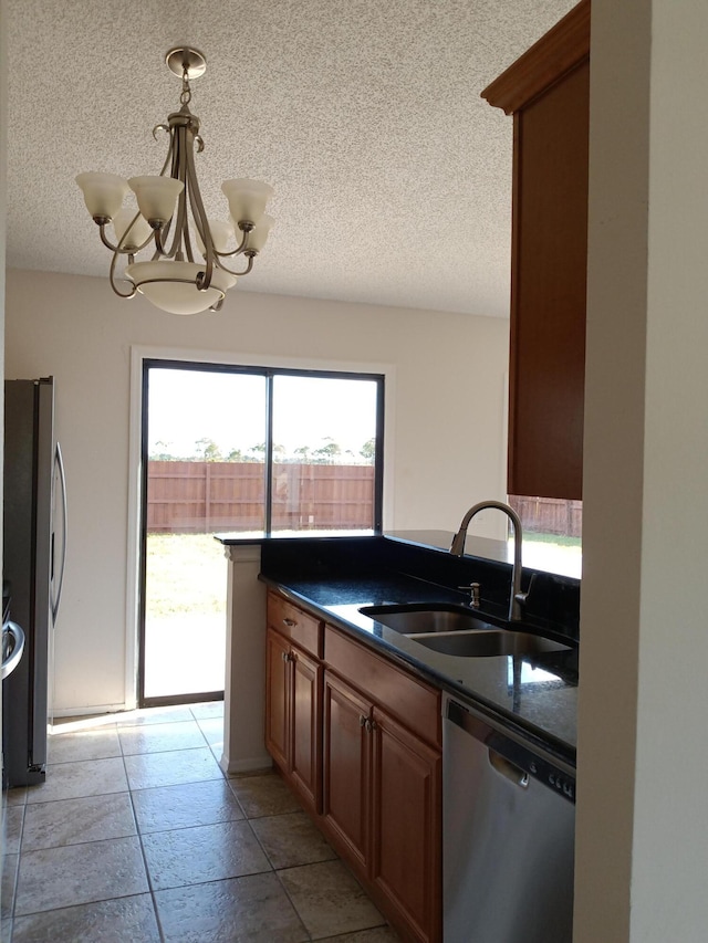 kitchen featuring a textured ceiling, stainless steel appliances, a sink, dark countertops, and an inviting chandelier