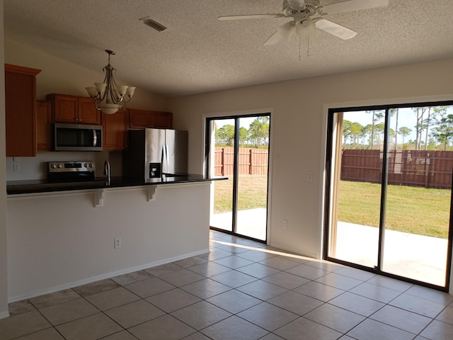 kitchen with light tile patterned floors, dark countertops, lofted ceiling, a peninsula, and stainless steel appliances