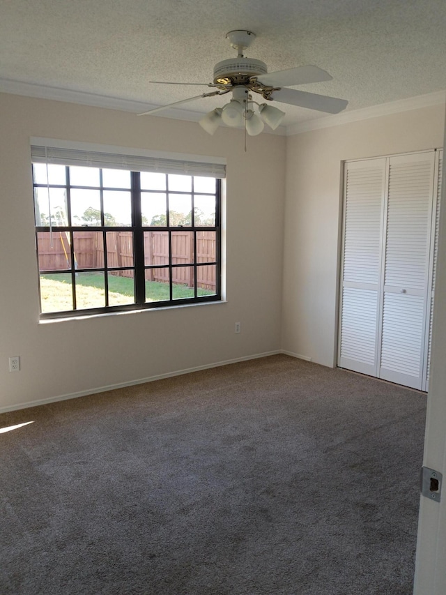 carpeted empty room featuring baseboards, a textured ceiling, a ceiling fan, and crown molding