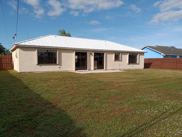 rear view of property with stucco siding, a fenced backyard, metal roof, and a yard