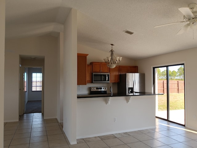 kitchen with dark countertops, visible vents, appliances with stainless steel finishes, brown cabinetry, and vaulted ceiling