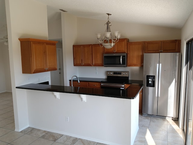 kitchen with dark countertops, appliances with stainless steel finishes, a peninsula, an inviting chandelier, and vaulted ceiling