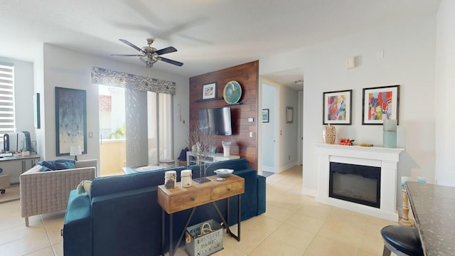 living area with light tile patterned floors, a glass covered fireplace, a ceiling fan, and baseboards