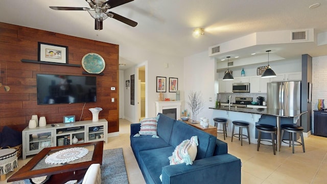 living room featuring ceiling fan, sink, wooden walls, a fireplace, and light tile patterned floors