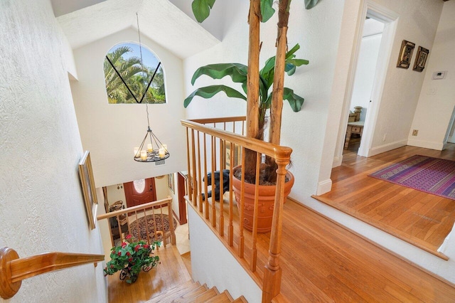 staircase featuring wood-type flooring, vaulted ceiling, and a notable chandelier