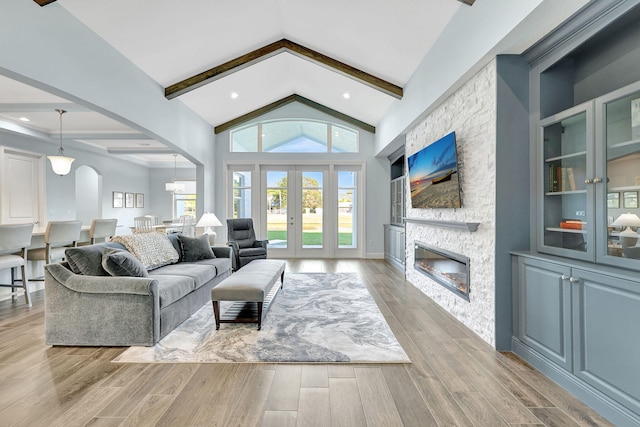 living room with light wood finished floors, high vaulted ceiling, a stone fireplace, and beam ceiling