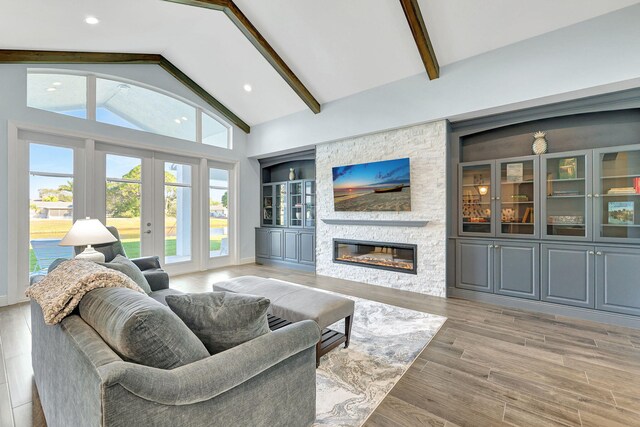 living area featuring a stone fireplace, built in shelves, light wood-style floors, french doors, and beamed ceiling