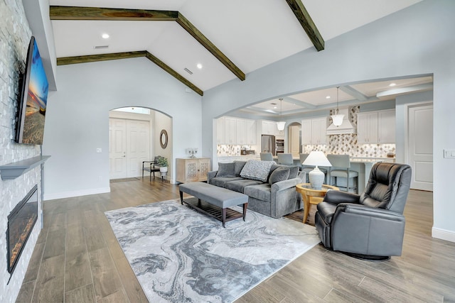 living area with arched walkways, high vaulted ceiling, light wood-style flooring, a fireplace, and beamed ceiling