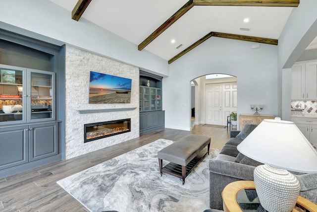 living room with beamed ceiling, wood-type flooring, high vaulted ceiling, and a fireplace