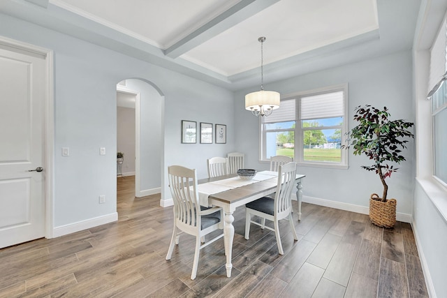 dining area featuring arched walkways, a tray ceiling, baseboards, and light wood-style floors