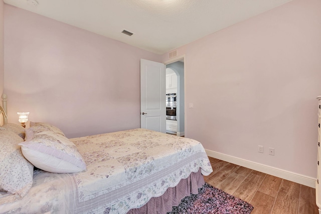 bedroom with baseboards, visible vents, and wood finished floors