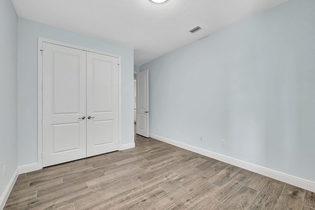 unfurnished bedroom featuring baseboards, a closet, visible vents, and light wood-style floors