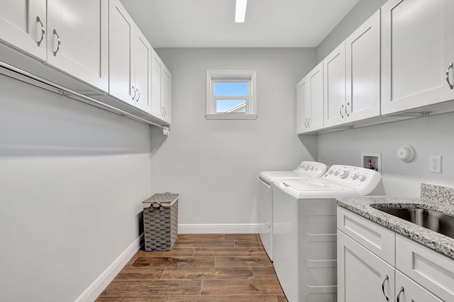 clothes washing area with cabinet space, baseboards, washer and clothes dryer, dark wood-style flooring, and a sink