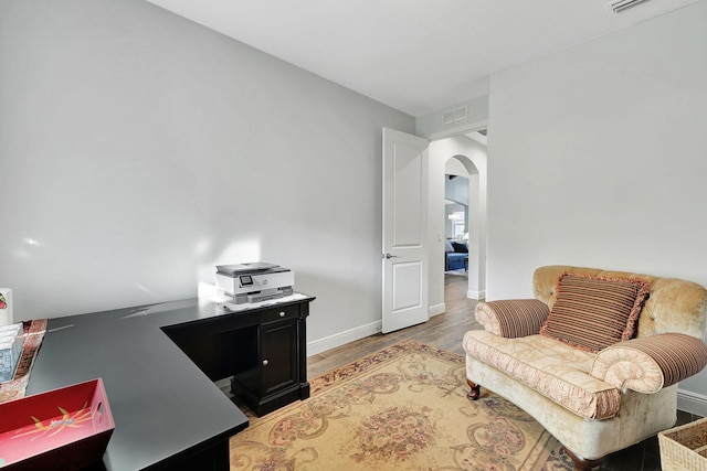 office space featuring light wood-type flooring, arched walkways, visible vents, and baseboards