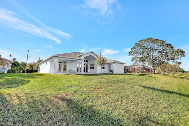 rear view of property with french doors, a lawn, and stucco siding