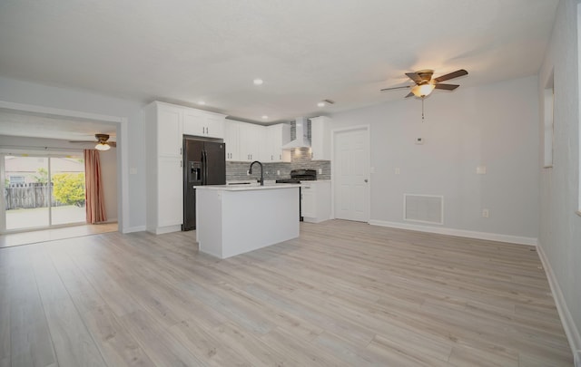 kitchen featuring light wood finished floors, visible vents, wall chimney exhaust hood, black refrigerator with ice dispenser, and backsplash