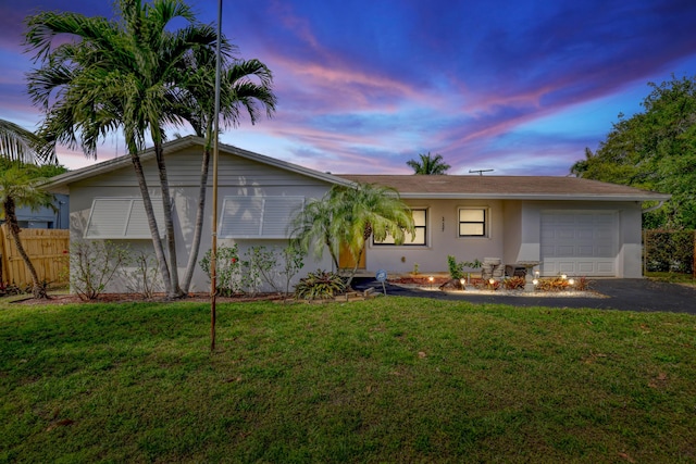 ranch-style house with aphalt driveway, fence, a front lawn, stucco siding, and an attached garage