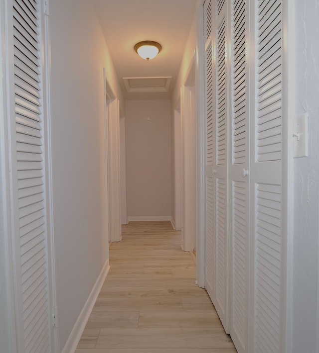 hallway with light wood-style flooring, attic access, and baseboards