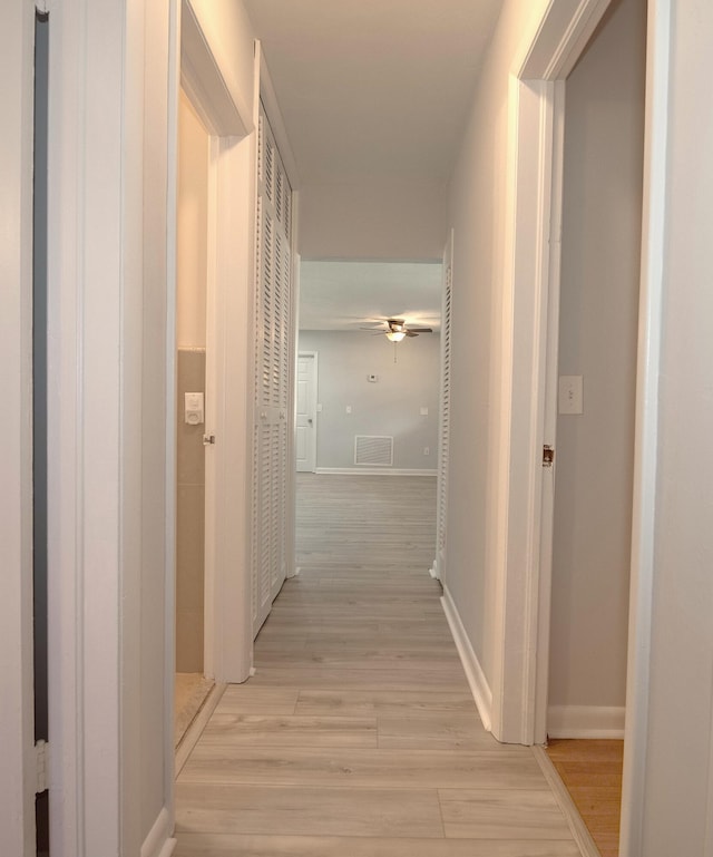 hallway featuring visible vents, light wood-style flooring, and baseboards