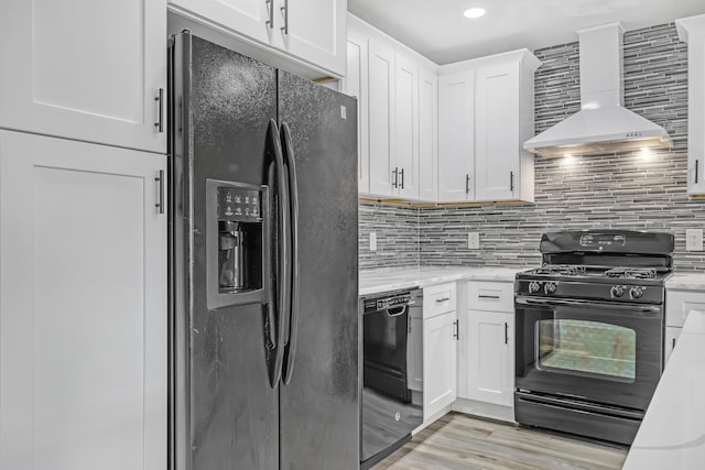 kitchen featuring black appliances, wall chimney exhaust hood, white cabinets, and backsplash