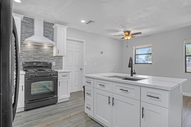 kitchen featuring decorative backsplash, light wood-style floors, black range with gas cooktop, a sink, and wall chimney exhaust hood