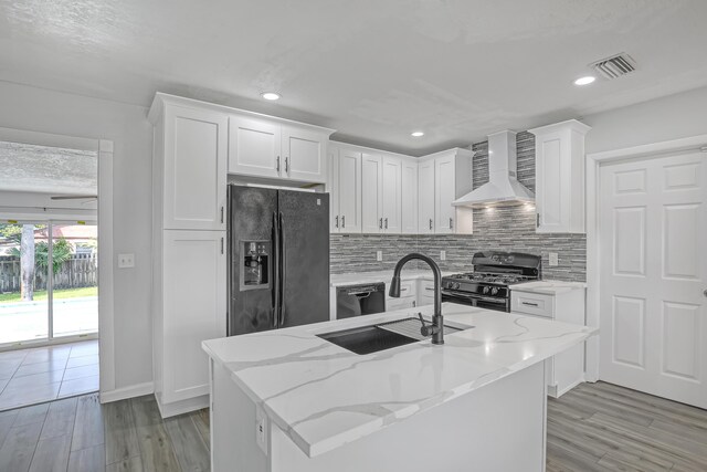 kitchen featuring visible vents, gas range oven, black fridge, wall chimney range hood, and a sink