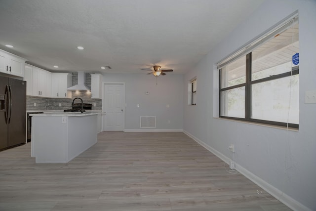 kitchen featuring visible vents, light countertops, black fridge, wall chimney exhaust hood, and tasteful backsplash