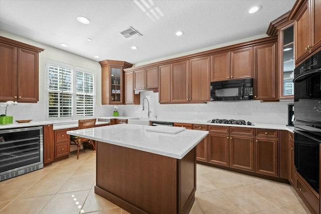 kitchen featuring a center island, sink, beverage cooler, light tile patterned flooring, and black appliances