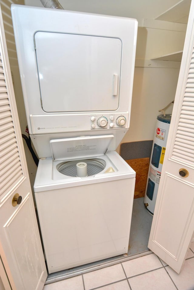 laundry area with light tile patterned flooring, stacked washer and dryer, and water heater