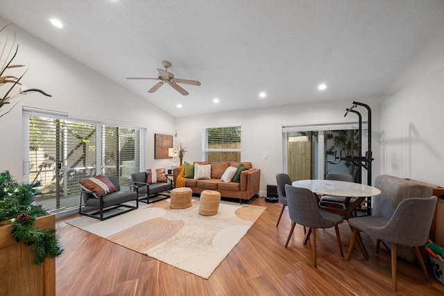 living room with a textured ceiling, ceiling fan, vaulted ceiling, and light wood-type flooring