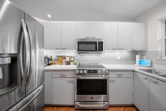 kitchen with white cabinets, stainless steel appliances, tasteful backsplash, and light hardwood / wood-style floors