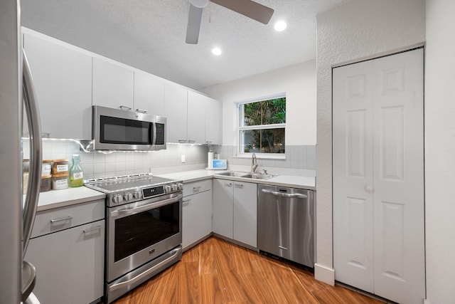 kitchen featuring appliances with stainless steel finishes, light wood-type flooring, a textured ceiling, sink, and white cabinetry