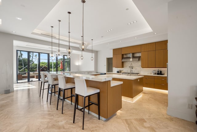 kitchen with decorative light fixtures, a large island, a raised ceiling, and wall chimney exhaust hood