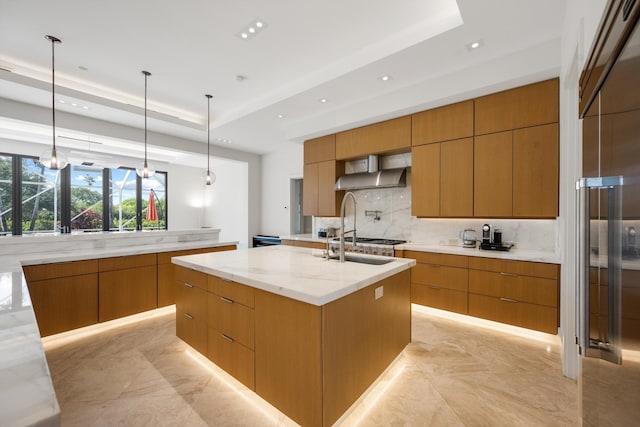 kitchen featuring light stone countertops, pendant lighting, a raised ceiling, a spacious island, and wall chimney range hood