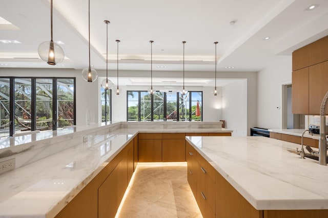 kitchen featuring light stone counters, a tray ceiling, and hanging light fixtures