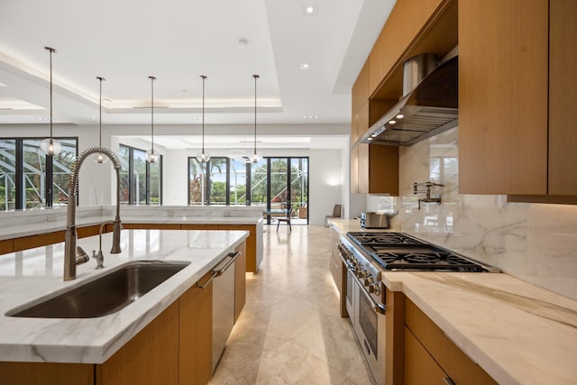 kitchen featuring hanging light fixtures, a raised ceiling, wall chimney range hood, appliances with stainless steel finishes, and sink