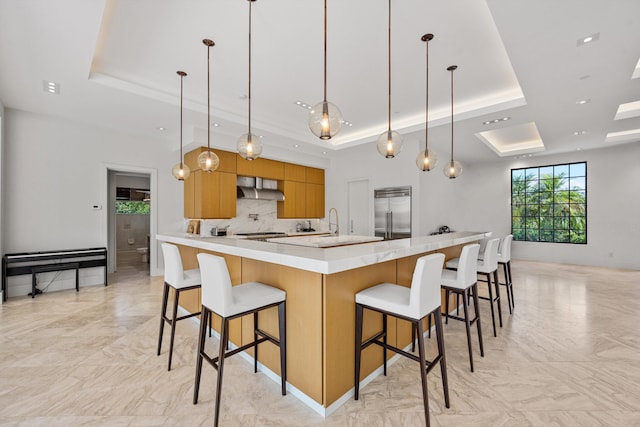 kitchen featuring range hood, a tray ceiling, decorative light fixtures, modern cabinets, and built in refrigerator