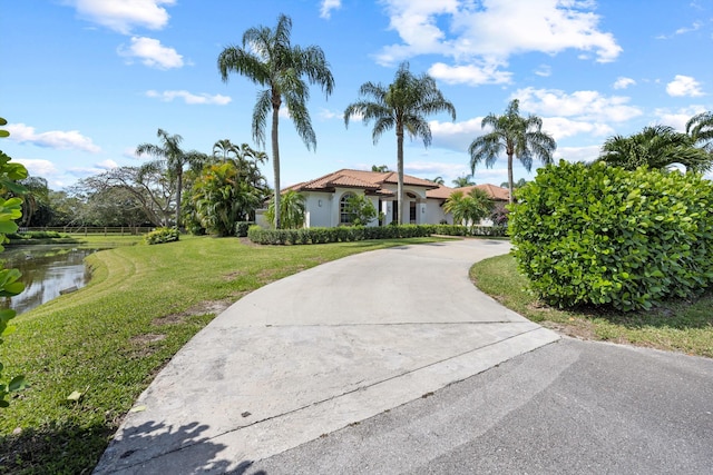 mediterranean / spanish home featuring a water view, a tile roof, concrete driveway, stucco siding, and a front lawn