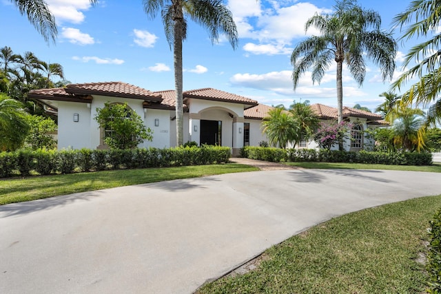 mediterranean / spanish home featuring concrete driveway, a front lawn, and stucco siding