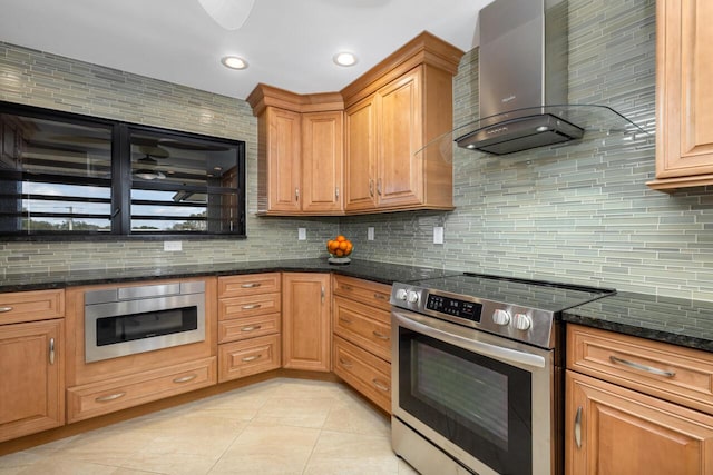 kitchen featuring appliances with stainless steel finishes, tasteful backsplash, wall chimney exhaust hood, and dark stone countertops