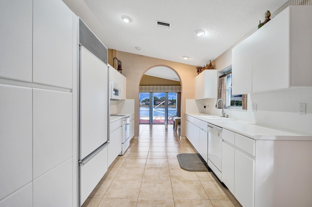 kitchen featuring sink, white cabinets, a textured ceiling, light tile patterned flooring, and white appliances