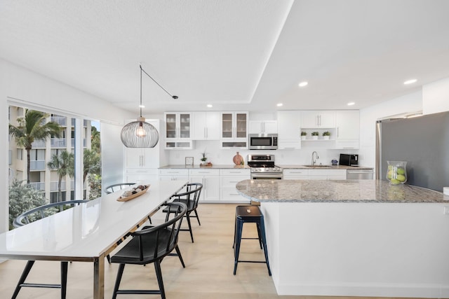 kitchen featuring white cabinets, decorative light fixtures, light stone countertops, and appliances with stainless steel finishes