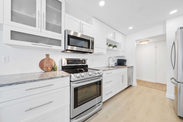 kitchen with light stone countertops, stainless steel appliances, sink, light hardwood / wood-style flooring, and white cabinetry