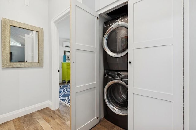 laundry room featuring stacked washing maching and dryer and light hardwood / wood-style flooring